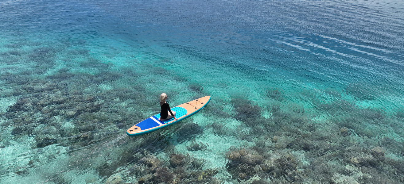 Person paddleboarding on a clear blue ocean with coral reef